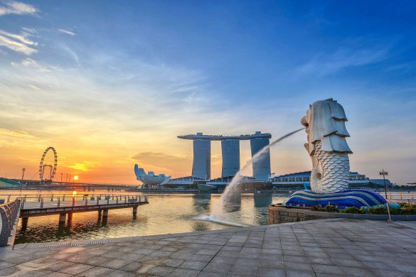 Blick auf den Merlion-Brunnen in Singapur bei Sonnenaufgang, mit Marina Bay Sands und Riesenrad im Hintergrund.