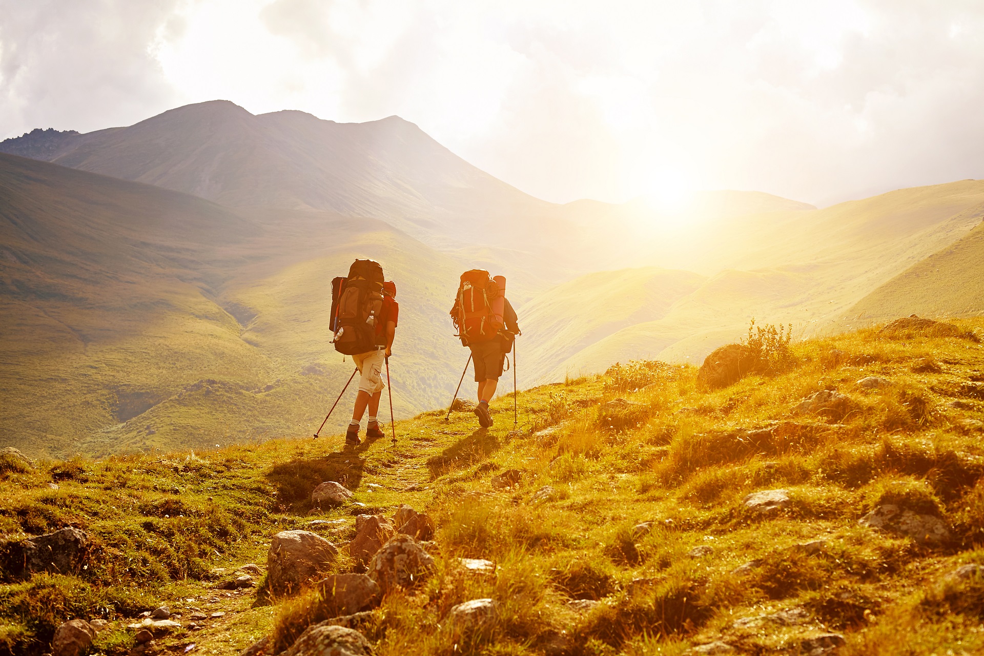 Wanderer laufen in Armeniens Hügellandschaft der untergehenden Sonne entgegen.