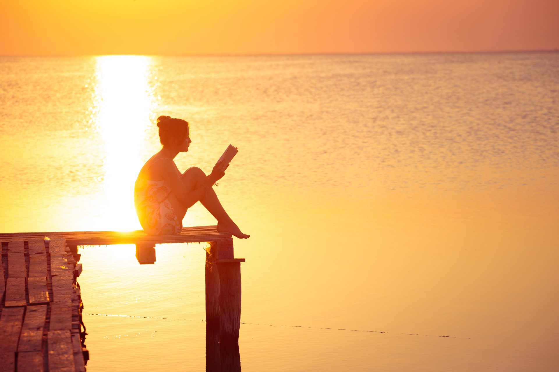 Frau liest bei Sonnenuntergang ein Buch auf einem Steg