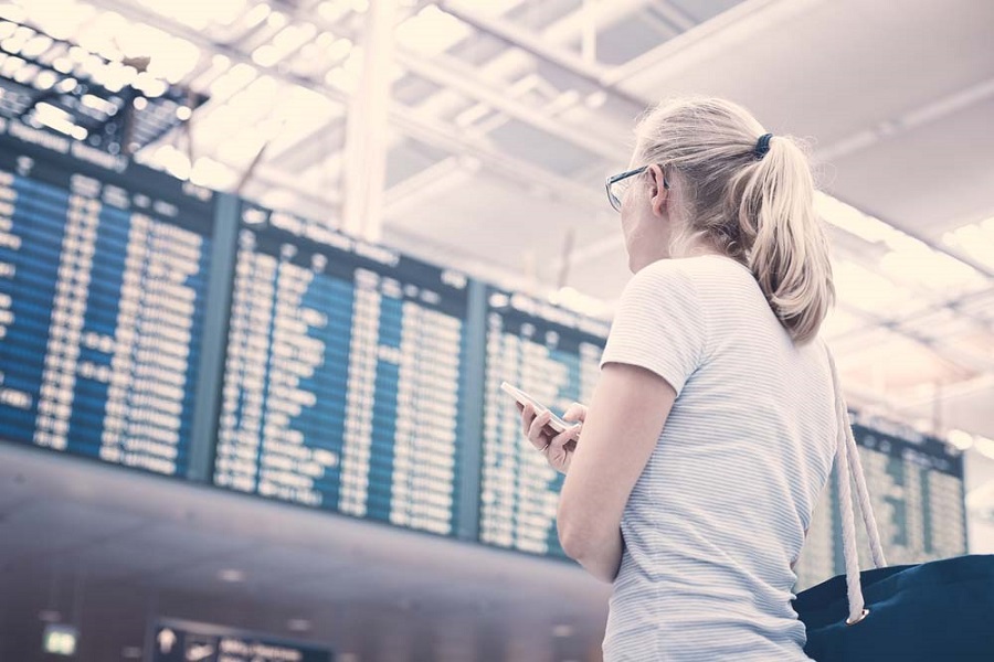 Frau steht am Flughafen und betrachtet die Abflugzeiten