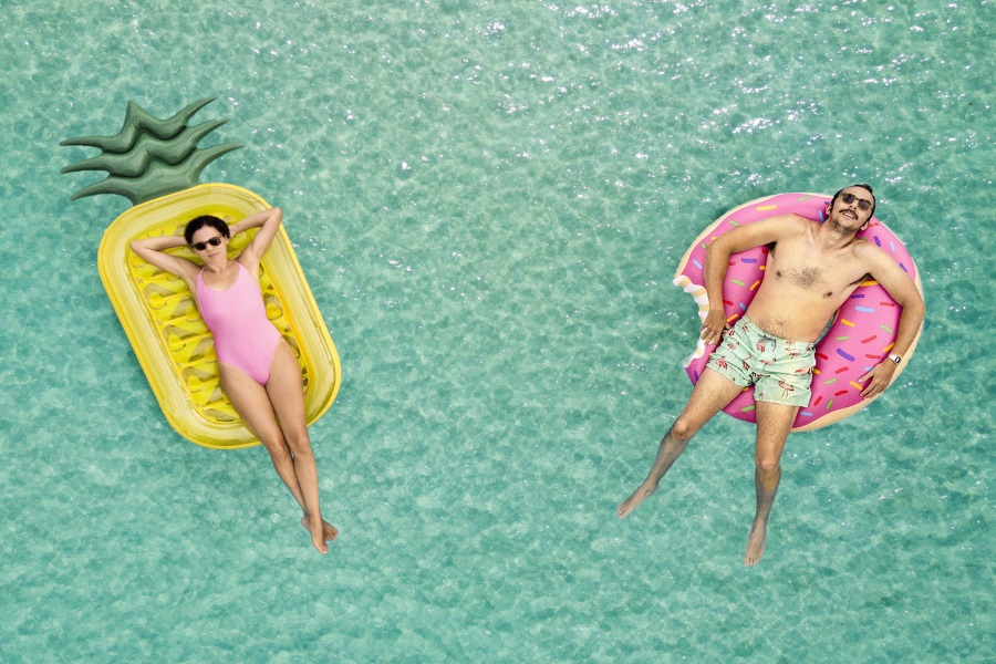 Ein Paar genießt zur Valentinstagszeit zu zweit entspannte Momente auf schwimmenden Luftmatratzen im klaren, türkisblauen Ozeanwasser.
