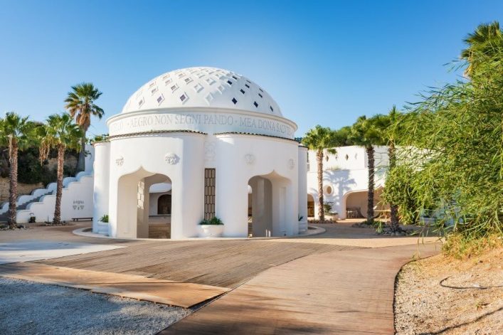 Weisses Kuppelgebäude der Kallithea-Therme auf Rhodos, umgeben von Palmen und mediterraner Vegetation, strahlend unter blauem Himmel.