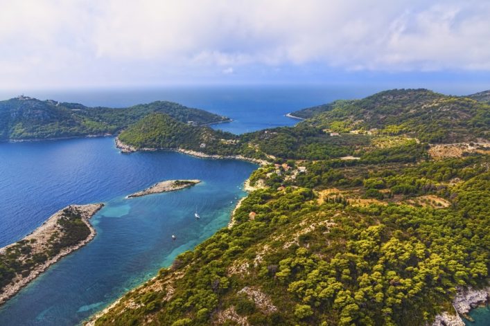 Blick auf die Insel Mljet in Kroatien mit üppiger grüner Vegetation im Vordergrund, türkisfarbenem Wasser in der Mitte und Hügeln im Hintergrund, die sich bis zum Horizont erstrecken.