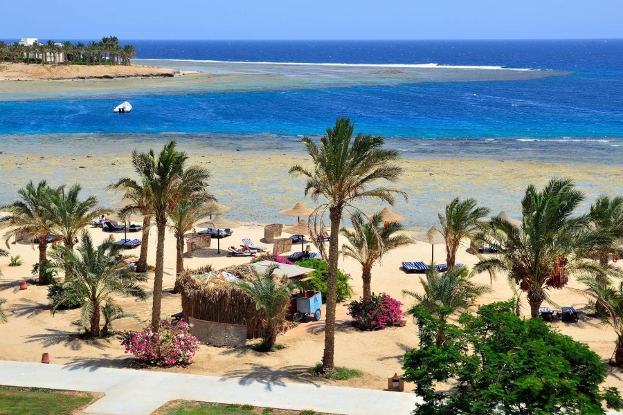 Palmengesäumter Sandstrand mit Liegestühlen, klarem blauen Meer in Marsa Alam, Ägypten, ideal für Ferien am Meer.