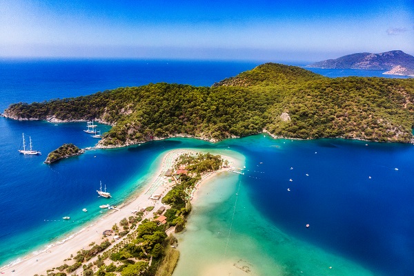 Türkisfarbenes Meer umschließt eine sandige Landzunge in der Türkei. Grüne Hügel rechts und Boote im Wasser ergänzen idyllischen Urlaub am Meer.