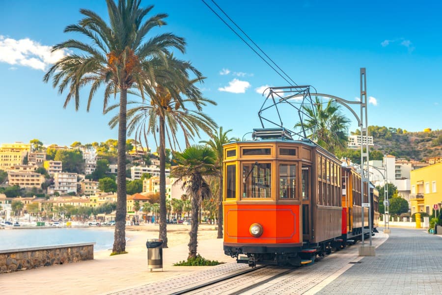 Historische Strassenbahn in Sóller, einer der Top 20 schönsten Orte auf Mallorca, umgeben von Palmen und Blick auf den Hafen.