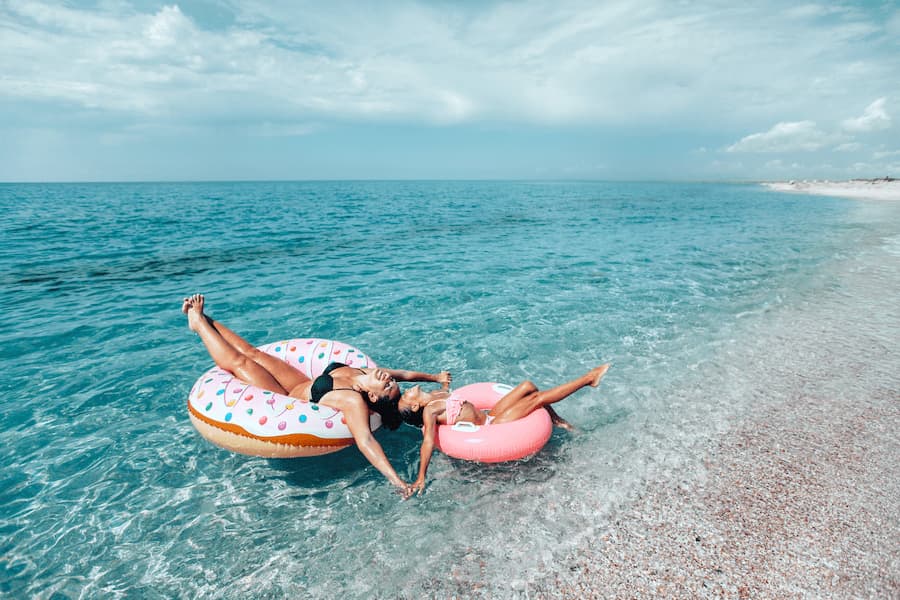 Eine Mutter und ihr Kind entspannen sich auf runden, aufblasbaren Schwimmringen im türkisblauen Meer. Sie halten sich an den Händen. Familienferien, die pure Erholung am sonnigen Strand bieten.