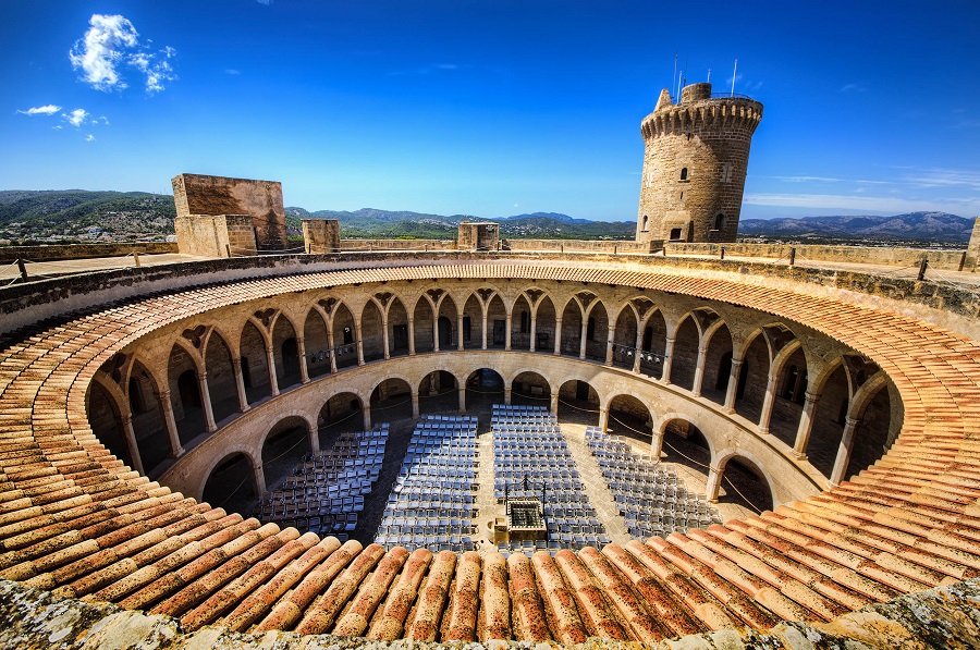 Das Castillo de Bellver in Palma de Mallorca mit seinem runden Innenhof und dem hohen Turm im Hintergrund ist eine faszinierende Sehenswürdigkeit für einen Familienurlaub auf Mallorca.