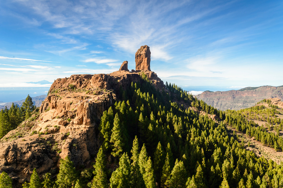 Majestätischer Roque Nublo auf Gran Canaria, umgeben von grünen Kiefernwäldern unter blauem Himmel.